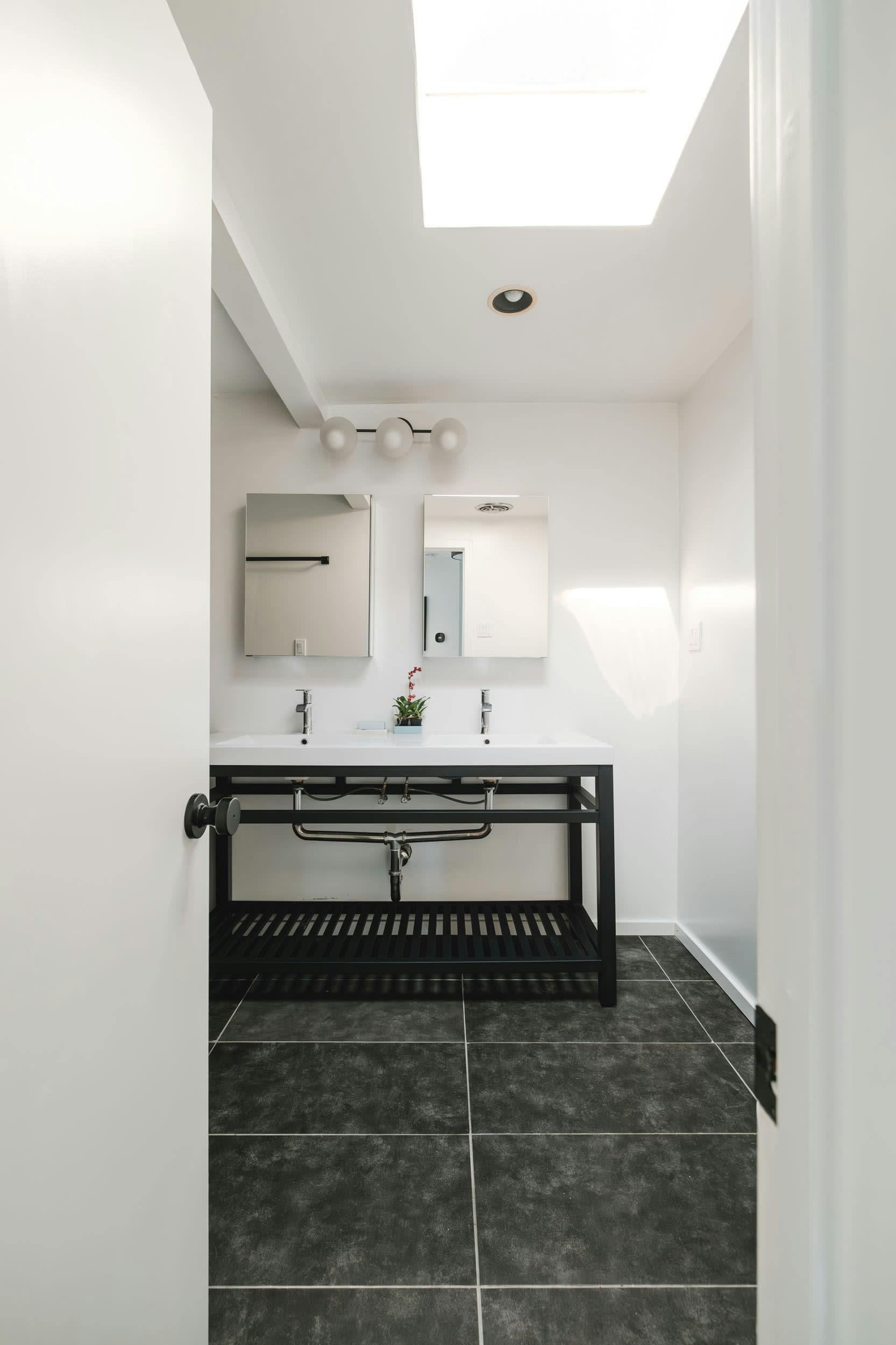 a black and white bathroom with a skylight above the sink and a black and white tiled floor and walls