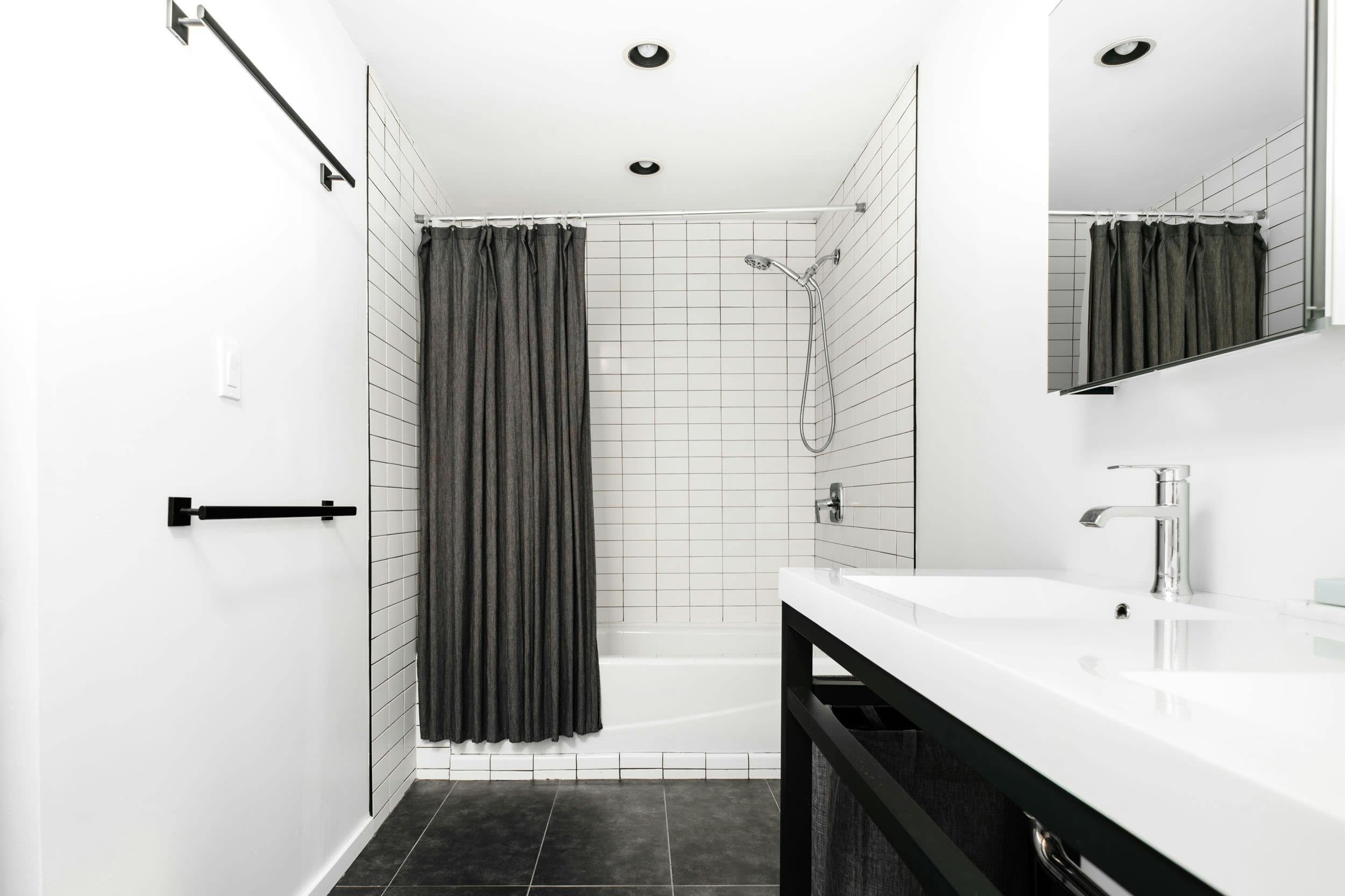 a black and white bathroom with a shower and a white sink and a black and white shower curtain and a black and white tiled floor