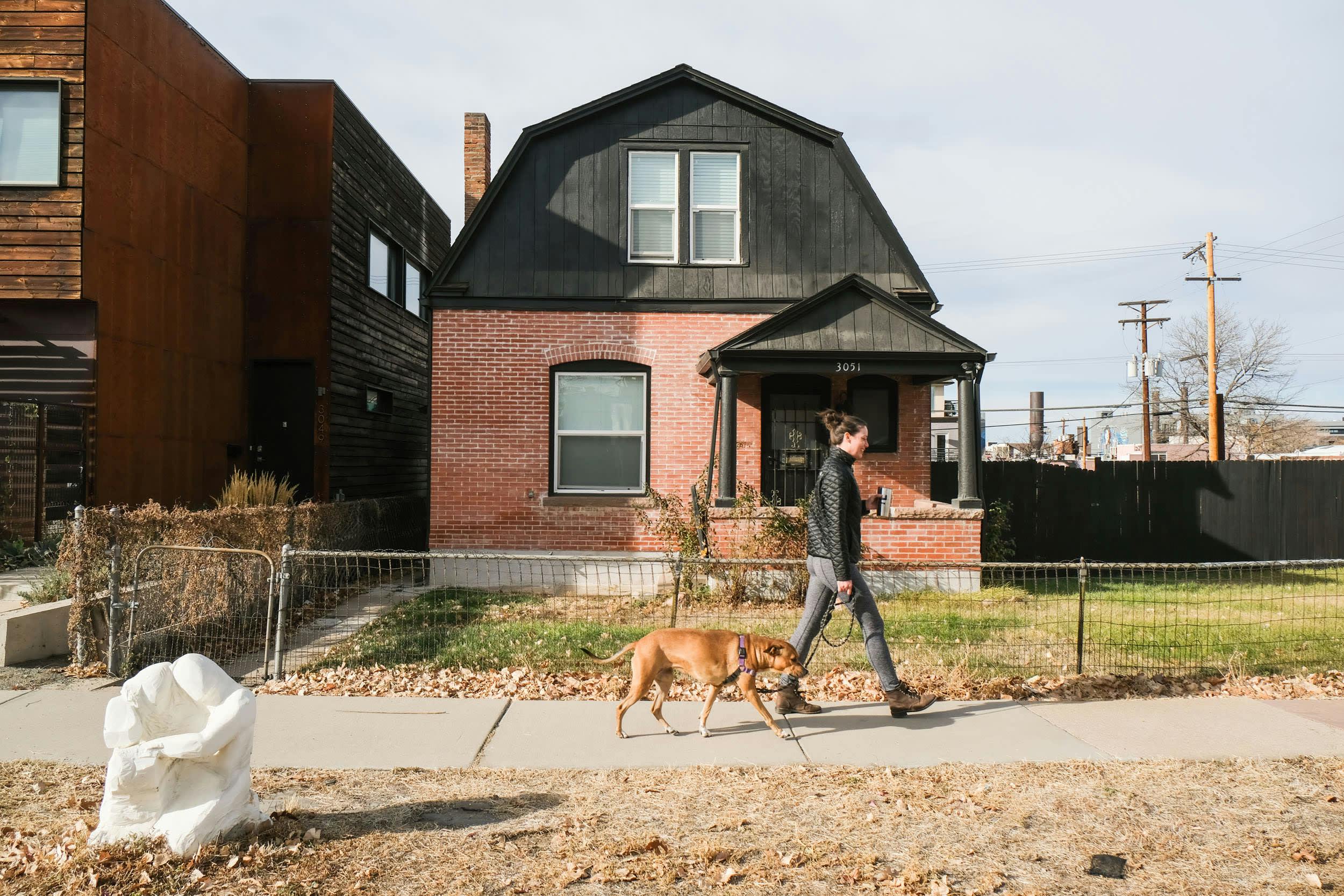 a man walking a dog on a sidewalk in front of a house with a fence and a fenced in yard