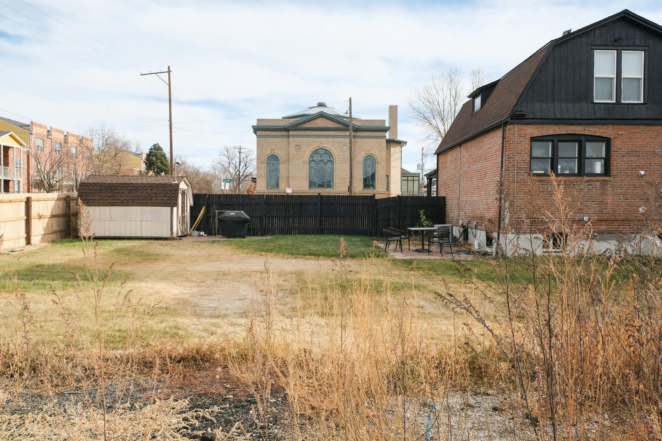 a vacant lot with a church in the background and a building in the foreground with tall grass in front of it