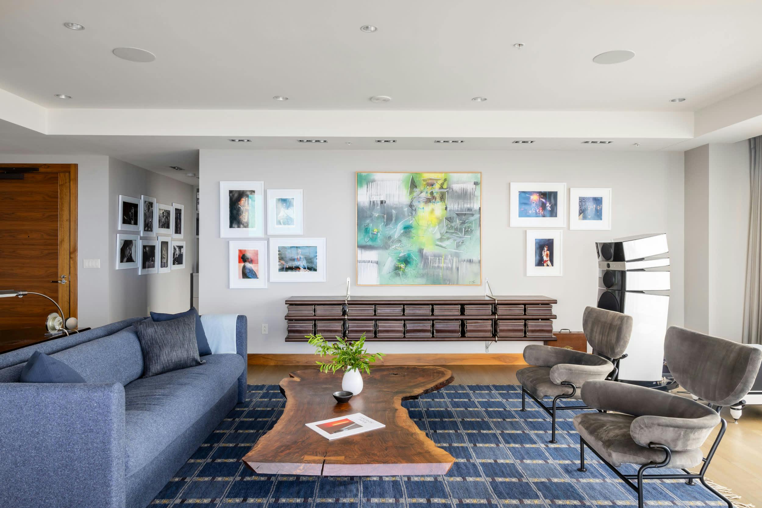 a living room filled with furniture and a painting on the wall above the couch and a coffee table on top of a blue rug