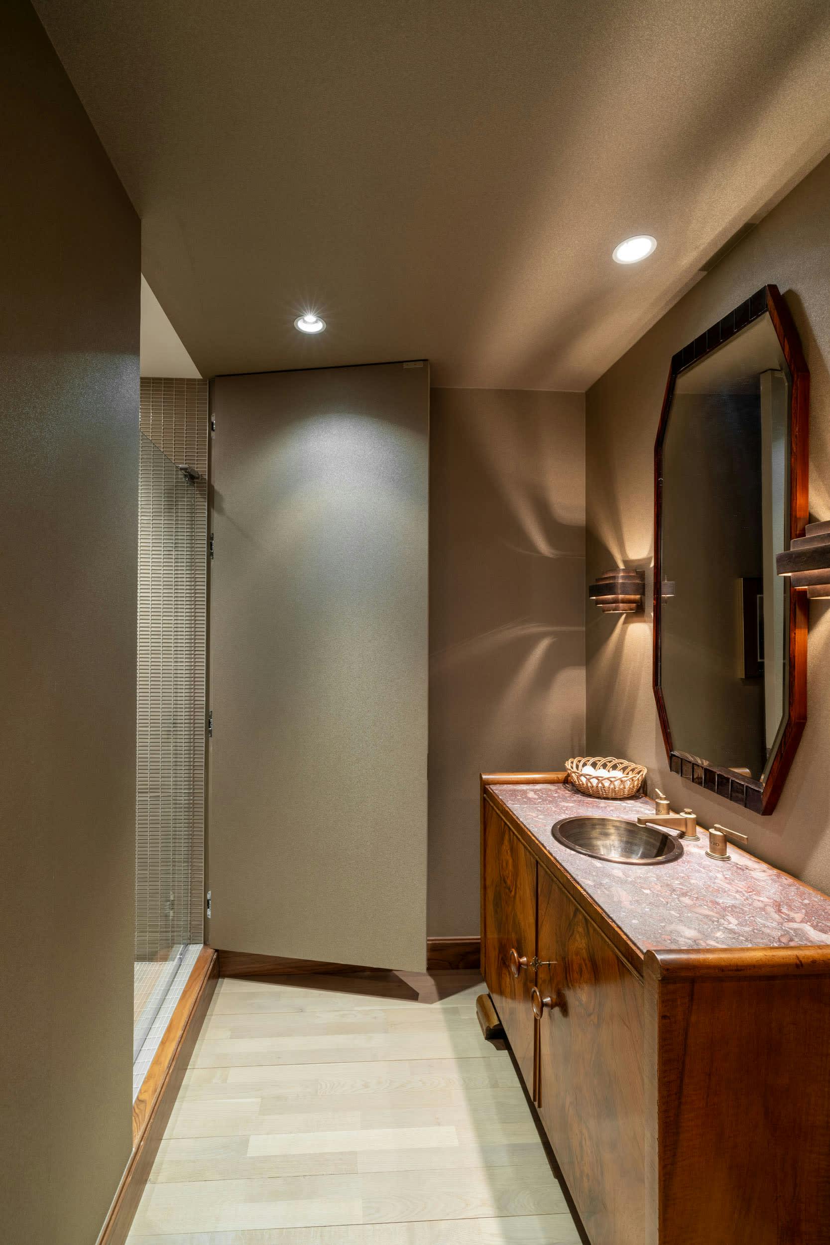 a bathroom with a sink, mirror, and shower stall with lights on the wall and a tiled floor