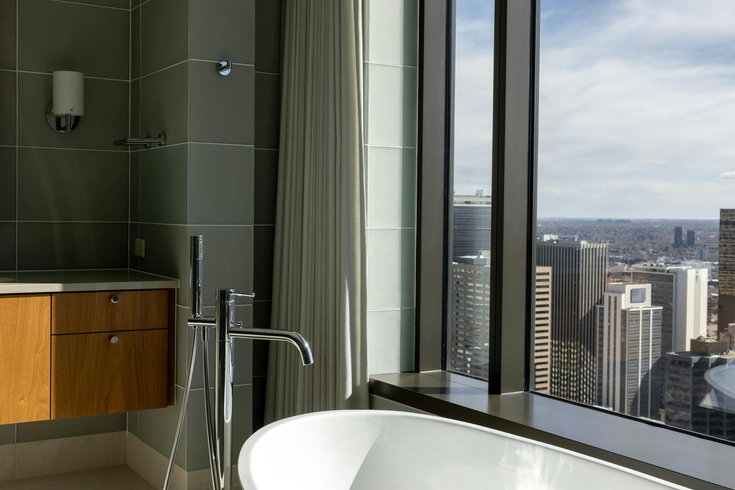 a bathroom with a tub, sink and large window overlooking a cityscape in the foreground, and a cityscape in the background