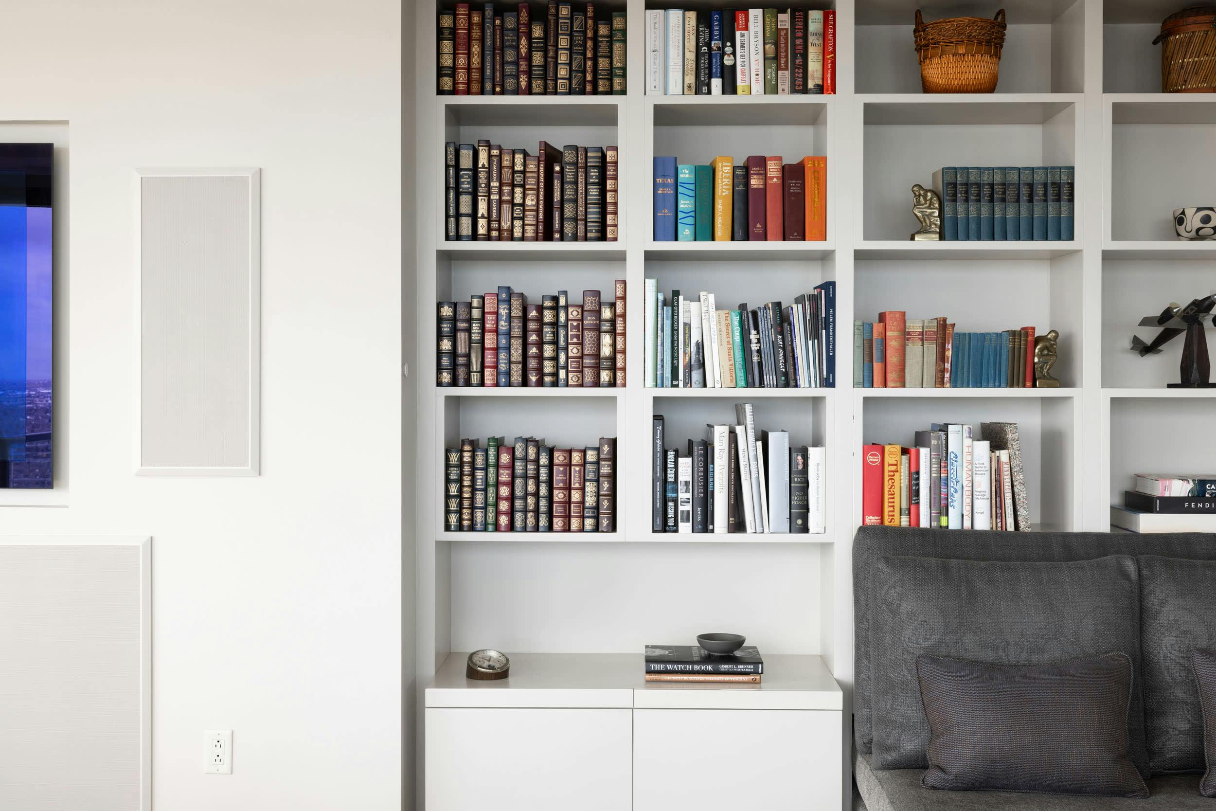 a living room with a couch and a book shelf filled with books and a television mounted to the wall