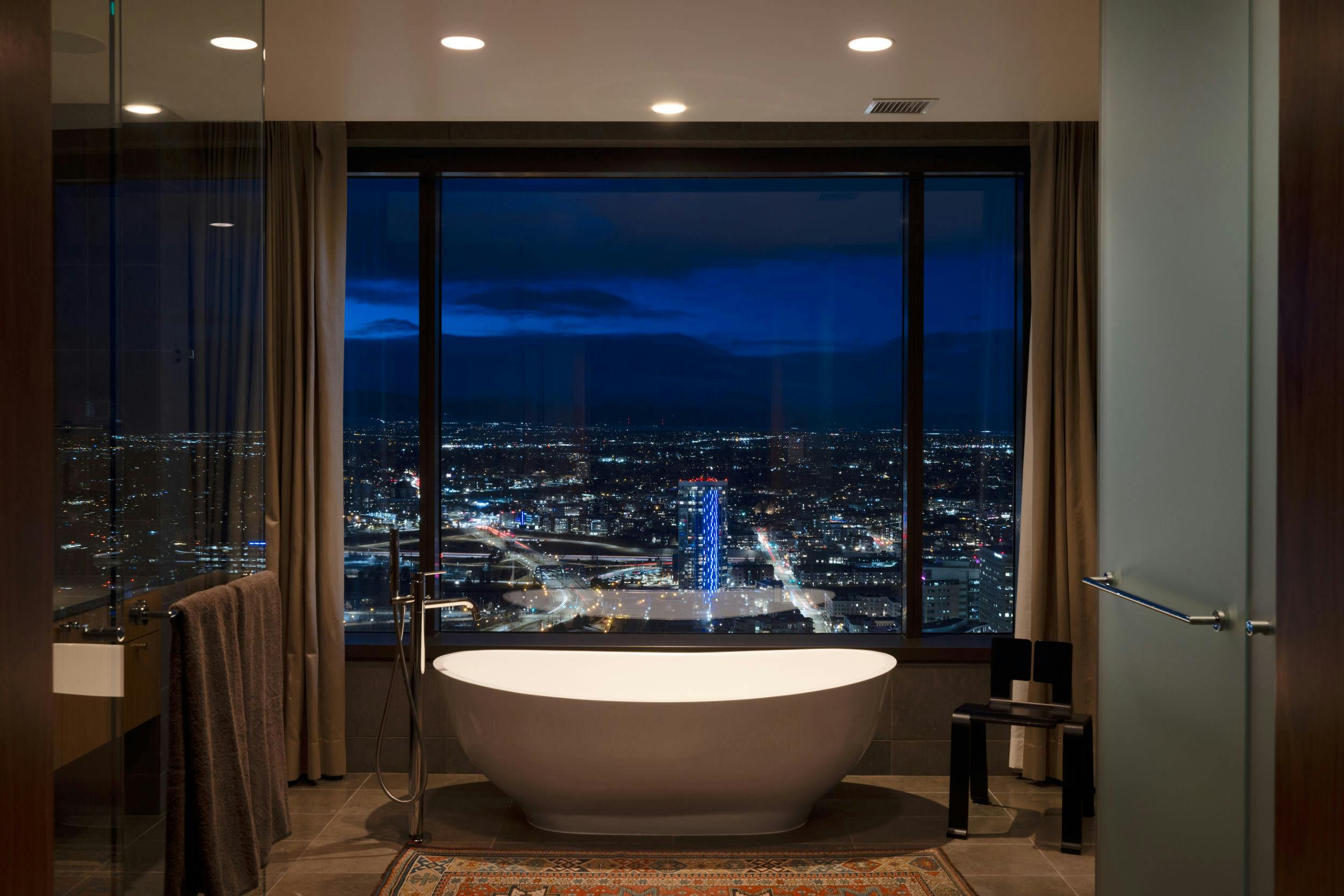 a bathtub in a bathroom with a view of a city at night from the window of a high rise building
