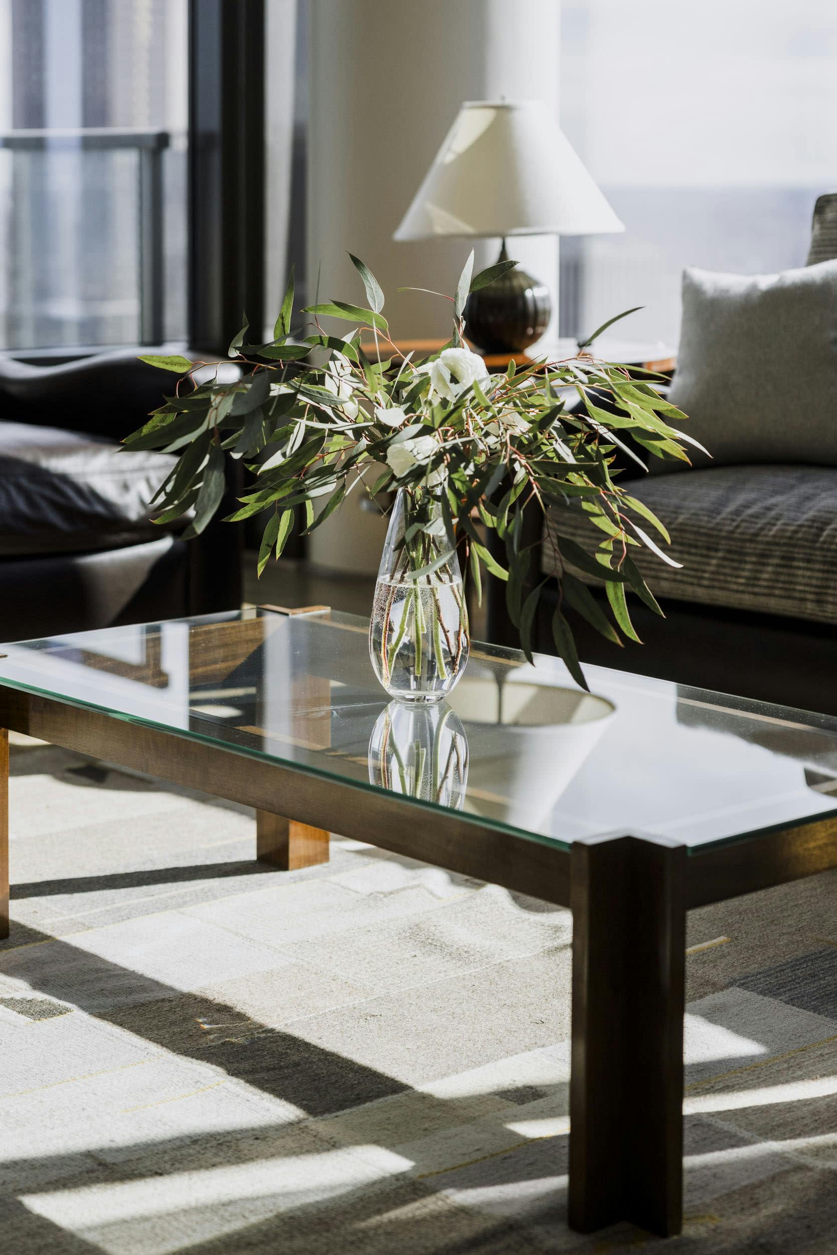 a glass table with a vase of flowers on top of it in front of a couch in a living room